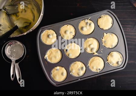 Moule à muffins doublé de papier d'emballage et rempli de pâte de macareux aux myrtilles : pâte de macareux aux myrtilles non cuite dans un moule à muffins avec outils de cuisine Banque D'Images