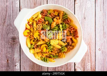 Pâtes tricolores égouttées dans un grand passoire : vue en hauteur de différentes formes de pâtes tricolores dans une passoire en plastique Banque D'Images