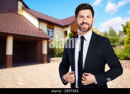 Un agent immobilier heureux près d'une belle maison à l'extérieur. Espace pour le texte Banque D'Images