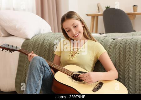 Adolescente jouant de la guitare acoustique près du lit dans la chambre Banque D'Images