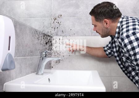 Homme regardant affecté avec des murs de moisissure dans la salle de bains Banque D'Images