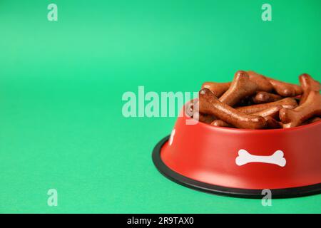 Bol rouge avec biscuits en forme d'os pour chiens sur fond vert. Espace pour le texte Banque D'Images