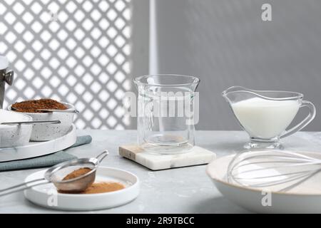Vider le verre, le lait, le tamis avec la poudre de cannelle et les granulés instantanés sur une table gris clair. Faire du café de Dalgona Banque D'Images
