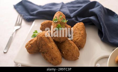 Boulettes de morue, ou « bolinhos de bacalhau » et feuilles de persil sur des plats en céramique blanche dans un comptoir de cuisine. Banque D'Images