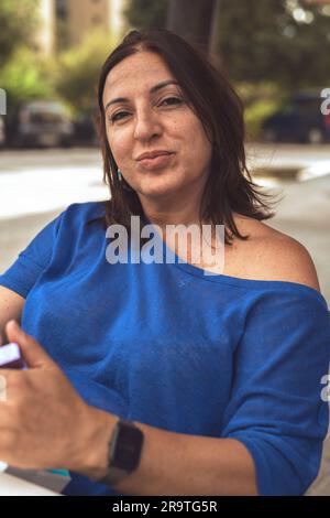 Portrait d'une femme brune dans un café, portant un chandail bleu et appréciant le cadre extérieur. Banque D'Images