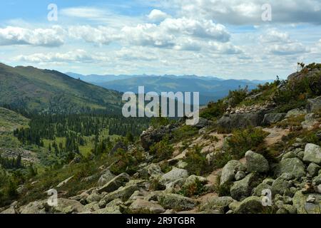 Une pente douce d'une montagne avec une dispersion de grandes pierres surplombant une vallée de montagne pittoresque lors d'une journée d'été nuageux. Parc naturel Ergaki Banque D'Images