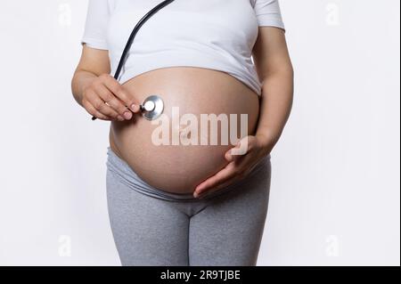 Gros plan la femme enceinte écoute le rythme cardiaque du futur bébé avec un stéthoscope. Obstétrique et gynécologie. Développement du fœtus Banque D'Images