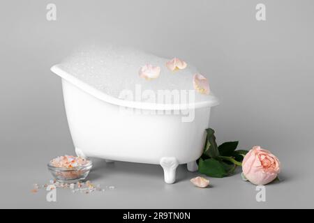 Petite baignoire avec mousse, sel de mer et fleur de rose sur fond clair Banque D'Images