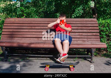 Garçon assis sur le banc et communique par chat vidéo à l'aide d'un smartphone et d'Internet. Banque D'Images