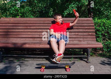 Garçon assis sur le banc et communique par chat vidéo à l'aide d'un smartphone et d'Internet. Banque D'Images