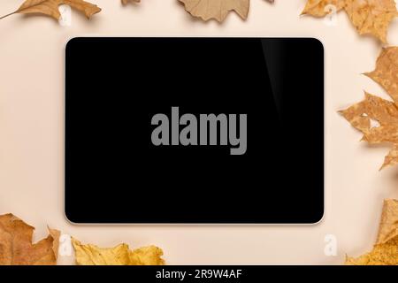 Tablette avec écran vierge sur une table entourée de feuilles d'automne nature, maquette parfaite Banque D'Images