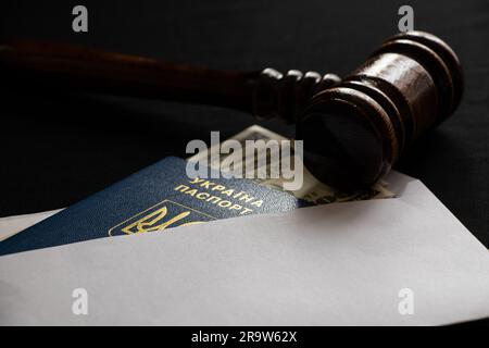 Un passeport ukrainien biométrique et des dollars dans une enveloppe et le gavel d'un juge se trouvent sur un fond noir, la loi et la corruption en Ukraine, le tribunal Banque D'Images