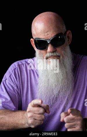 Portrait d'un homme avec une longue barbe grise portant un t-shirt violet et des lunettes de soleil montrant les doigts à l'appareil photo Banque D'Images