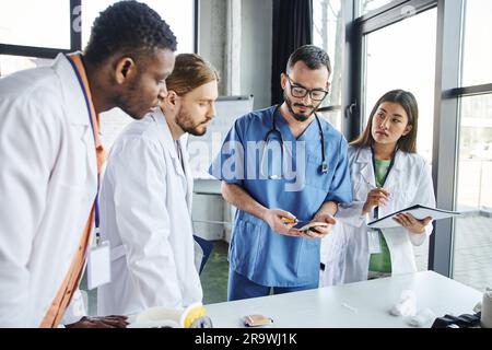 professionnel paramédical pratiquant avec le bloc d'injection près de divers groupes d'étudiants multiculturels en manteaux blancs pendant le séminaire médical dans la formation ro Banque D'Images