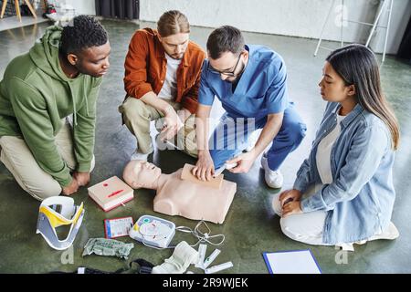 séminaire de premiers soins, vue en grand angle de la plaie de tamponnage paramédical sur simulateur avec bandage près de l'équipe multiethnique et de l'équipement médical, ski de sauvetage Banque D'Images