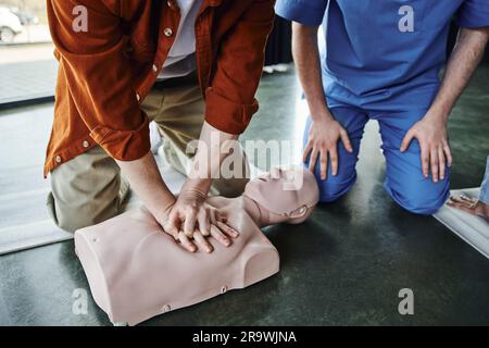 Vue partielle d'un jeune homme effectuant des compressions thoraciques sur un mannequin de RCP pendant un séminaire de premiers soins près d'une réanimation cardio-pulmonaire professionnelle, Banque D'Images