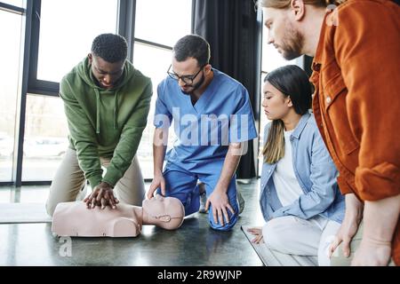 Jeunes multiethniques et instructeur médical regardant l'homme afro-américain faisant des compressions thoraciques sur mannequin de RCP, réanimation cardio-pulmonaire Banque D'Images