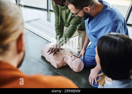 afro-américain homme pratiquant des compressions thoraciques et la réanimation cardiopulmonaire sur mannequin de RCP près d'un instructeur médical et de jeunes participants de Banque D'Images