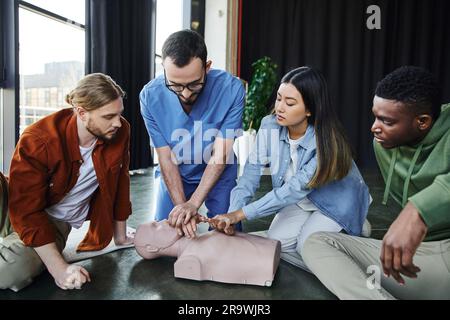 Formation aux premiers soins, instructeur médical montrant la réanimation cardiopulmonaire sur mannequin de RCP près de participants multiethniques dans la salle de formation, efficace Banque D'Images