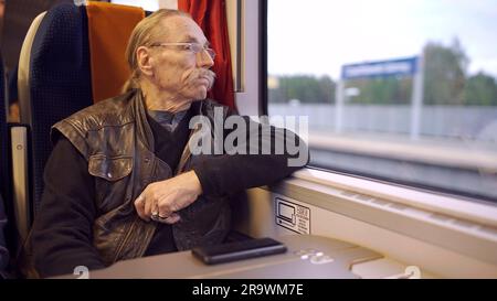 Gros plan d'un senior avec des lunettes voyage dans un train et regarde par la fenêtre Banque D'Images