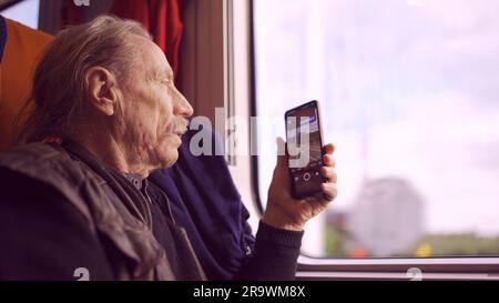 Homme âgé voyageant en train et prenant des photos du paysage par la fenêtre à l'aide d'un smartphone Banque D'Images