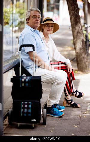 Un couple plus âgé vêtu de vêtements d'été avec un chariot attendant un bus à un arrêt de bus, Cologne, Rhénanie-du-Nord-Westphalie, Allemagne Banque D'Images