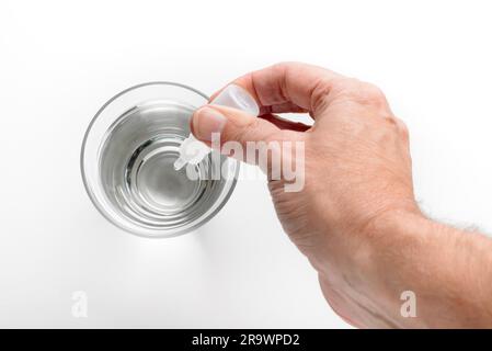 La main de l'homme mettre gouttes de réputation dans un verre d'eau transparente, sur fond blanc Banque D'Images