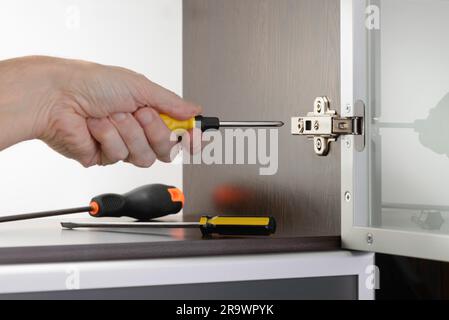 Un homme utilise un tournevis pour régler une charnière dissimulée fixé sur un cabinet moderne avec une porte en verre Banque D'Images