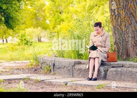 Femme élégante assise sur un mur de pierre au cours d'une journée de printemps ensoleillée, et la lecture d'un livre d'aventure Banque D'Images