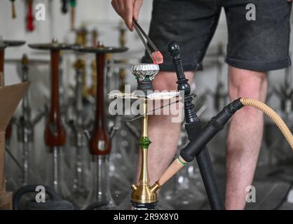 Sindelfingen, Allemagne. 29th juin 2023. Un morceau de charbon pour chauffer le tabac est placé sur un tuyau d'eau de nargua dans un bar de nargua. Les bars de shisha dominent de plus en plus le paysage urbain dans de nombreuses villes. Mais le marché du narguilé souffre de trop de règles et de bureaucratie, critiquant les jeunes libéraux du Bade-Wurtemberg. (À dpa "les jeunes libéraux critiquent la bureaucratie pour les barres de nargua") Credit: Bernd Weißbrod/dpa/Alamy Live News Banque D'Images