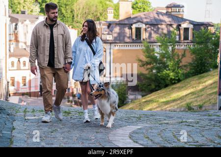 Un jeune couple marche avec son berger australien en zone urbaine. Un homme et une femme heureux marchent leur animal de compagnie dans la ville, un vrai mode de vie Banque D'Images