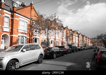 Fulham, Londres- rangée de maisons en terrasses typiques de briques rouges avec ciel et route détourrés Banque D'Images