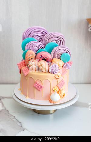 Gâteau rose décoré avec des sucettes colorées, des beignets, des popsicles, des tourbillons de meringue, des barres de chocolat et des étoiles dorées Banque D'Images