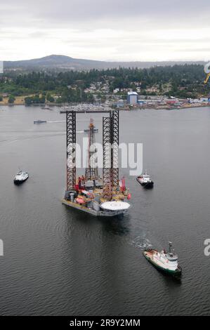 Image aérienne d'un engin de forage pétrolier remorqué hors du port par trois remorqueurs. Banque D'Images