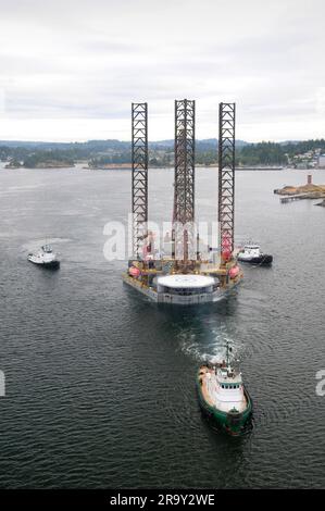 Image aérienne d'un engin de forage pétrolier remorqué hors du port par trois remorqueurs. Banque D'Images