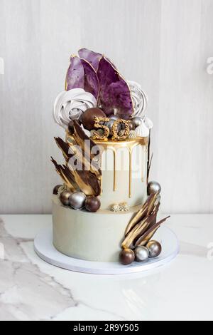 Grand gâteau gris et doré élégant à deux couches pour un anniversaire d'homme, décoré d'isomalt, de meringues, de sphères de chocolat et de pétales Banque D'Images