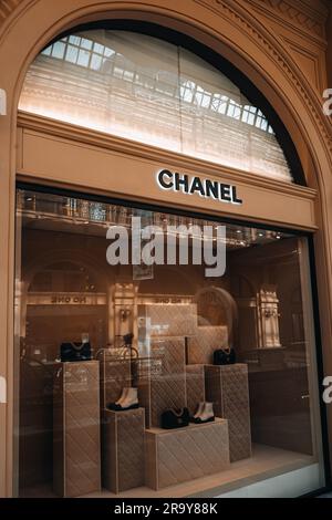 L'entrée de la boutique Chanel est chic et esthétique. Support beige neutre avec sac à main noir et chaussures blanches dans la fenêtre d'un magasin de luxe. Marque haute couture Banque D'Images