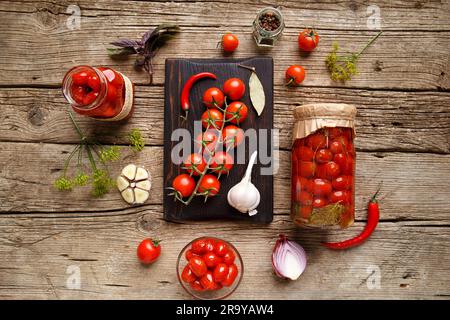 Tomates cerises en conserve en pots ouverts et fermés, ingrédients pour la conservation, une branche de tomates fraîches, poivrons, ail sur fond de bois vieilli Banque D'Images