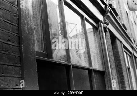 Whitechapel Londres dans une route juste à côté de Brick Lane, une femme asiatique solitaire regarde par sa fenêtre plate. La presse a rapporté que de nombreux nouveaux immigrants en Grande-Bretagne, et en particulier les femmes bangladaises, étaient tenus sous clé par leurs hommes. Ils ne parlaient pas la langue et étaient rarement autorisés à sortir de chez eux. Whitechapel, Londres, Angleterre 1978. Banque D'Images