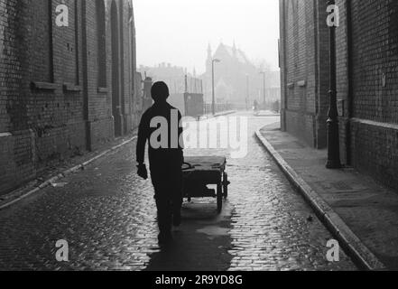 Whitechapel East London 1970s. L'homme de la classe ouvrière tire une charrette le long de la rue pavée devant d'énormes entrepôts sans fenêtres. Au loin se trouve l'église St Annes. la zone a été complètement réaménagée. Tower Hamlets, Londres, Angleterre circa 1974 70s UK HOMER SYKES Banque D'Images