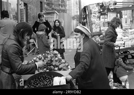 Châtaignes grillées chaudes Londres 1970s. Négociant sur le marché de Roman Road, vend des châtaignes grillées chaudes et des pommes de caramel avec un extérieur de caramel dur et cassant. Ils sont protégés par un emballage en cellophane transparent résistant. Tower Hamlets, Londres, Angleterre 1975 Royaume-Uni HOMER SYKES Banque D'Images