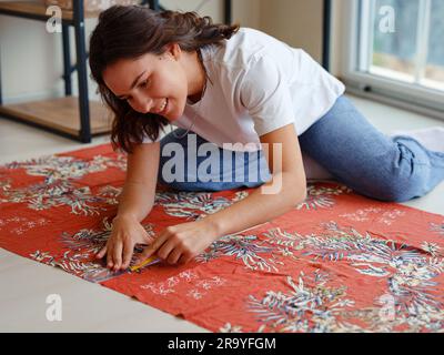 Jeune femme concentrée découpe sur mesure avec motif en ciseaux sur les lignes d'esquisse pour la machine à coudre. Lieu de travail d'une commode. Concep fait main Banque D'Images