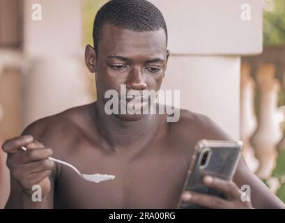 Photo sélective d'un jeune homme afro-américain qui mange et regarde son téléphone Banque D'Images