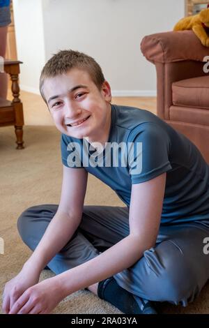 garçon de 15 ans assis à pieds croisés sur le sol d'un salon souriant. (M.) Banque D'Images
