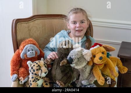 Portrait d'une jeune fille de 7 ans assise dans un fauteuil entouré d'animaux en peluche (MR) Banque D'Images