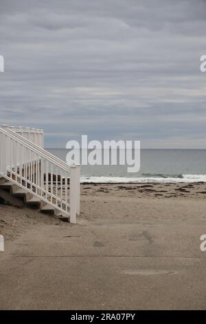 Escalier blanc menant à la plage de sable et à l'eau de l'océan avec ciel couvert Banque D'Images