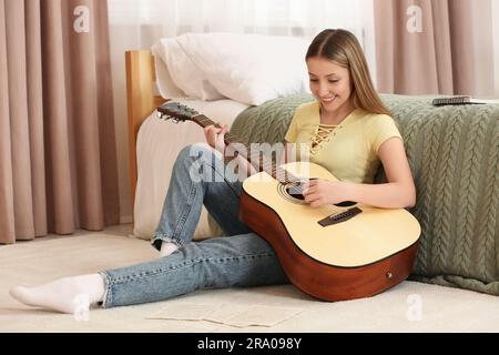 Adolescente jouant de la guitare acoustique près du lit dans la chambre Banque D'Images