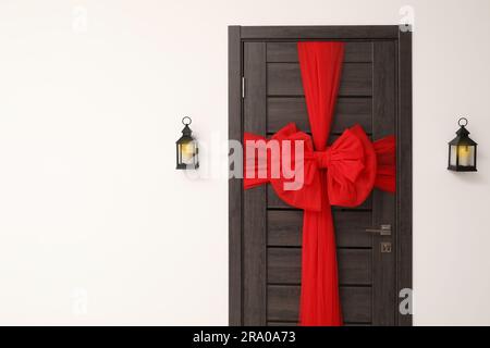 Porte en bois avec beau noeud rouge et lanternes accrochées au mur, espace pour le texte. Décoration de Noël Banque D'Images