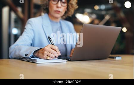 femme d'affaires écrit une liste de choses à faire sur un bloc-notes, planifiant sa semaine de travail. Femme d'affaires professionnelle travaillant à partir d'une table dans un espace de coworking. Banque D'Images