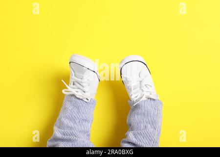 Petit bébé dans des chaussons élégants sur fond jaune, vue du dessus. Espace pour le texte Banque D'Images